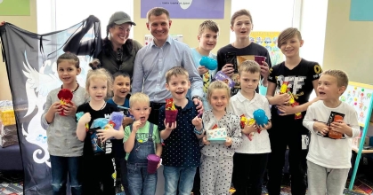 Представники «Saules Smiltys» Марія та Гедріус разом із усміхненими маріупольськими дітлахами позують для фото